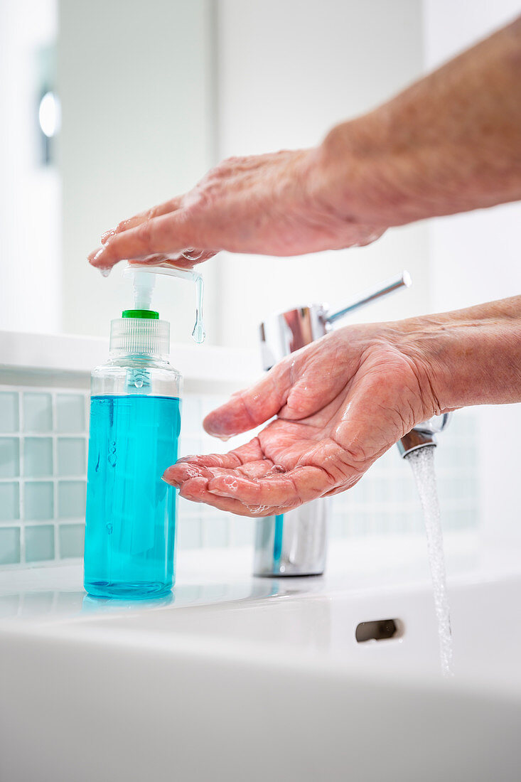 Senior woman washing hands with soap at bathroom sink