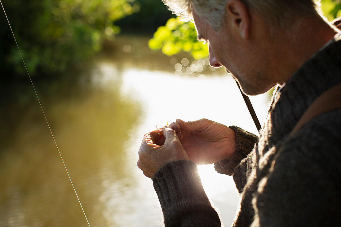 Man preparing fly fishing fly at sunny river