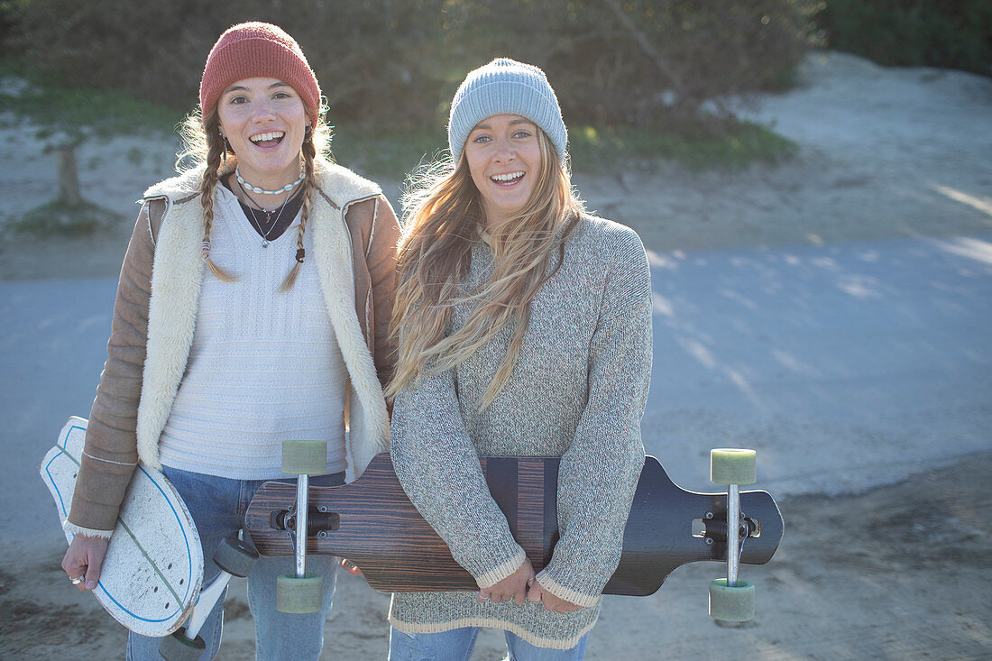 Happy young women friends in knit hats with skateboards
