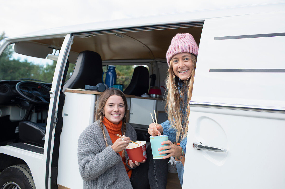 Happy young women friends eating instant noodles in van