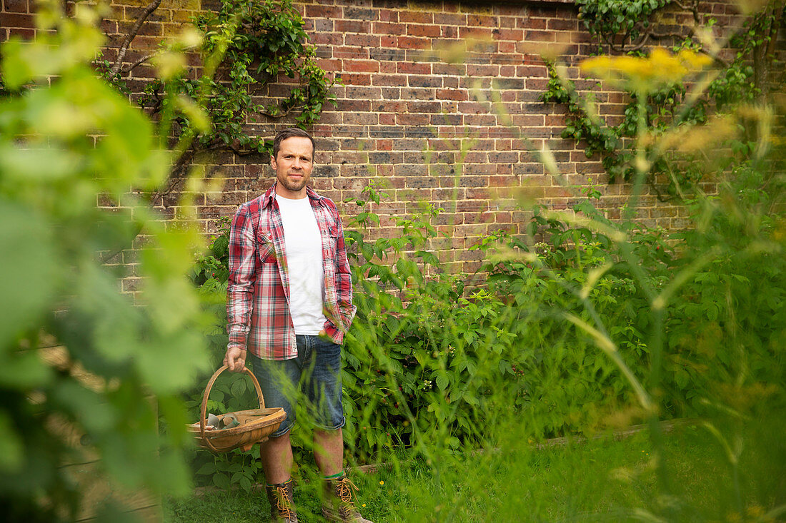 Confident man with basket at brick wall in summer garden