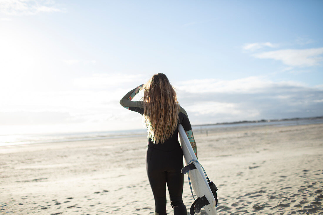 Young female surfer with surfboard on sunny beach