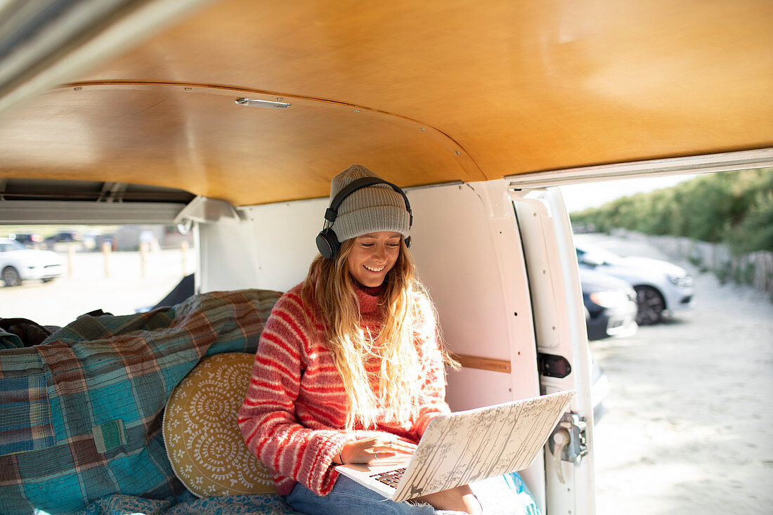 Happy young woman using headphones and laptop in camper van