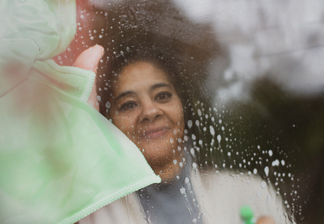 Smiling woman cleaning window with glass cleaner and rag