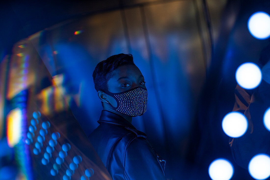 Young woman in studded face mask at dark mirror