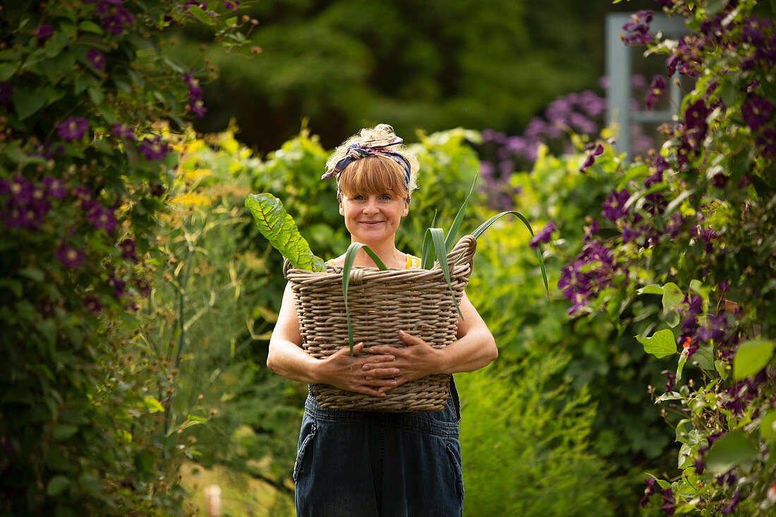 Happy woman with basket of harvested vegetables in garden