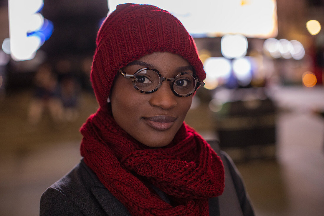 Confident young woman in eyeglasses scarf and hat at night