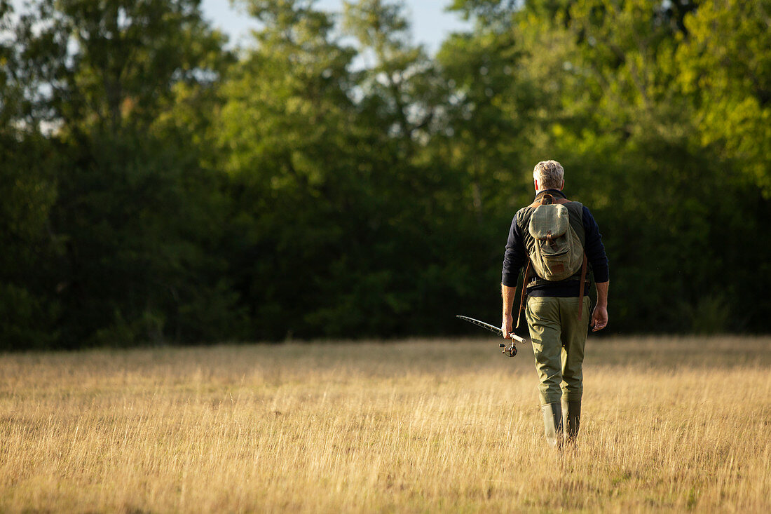 Man with backpack and fly fishing pole walking in field