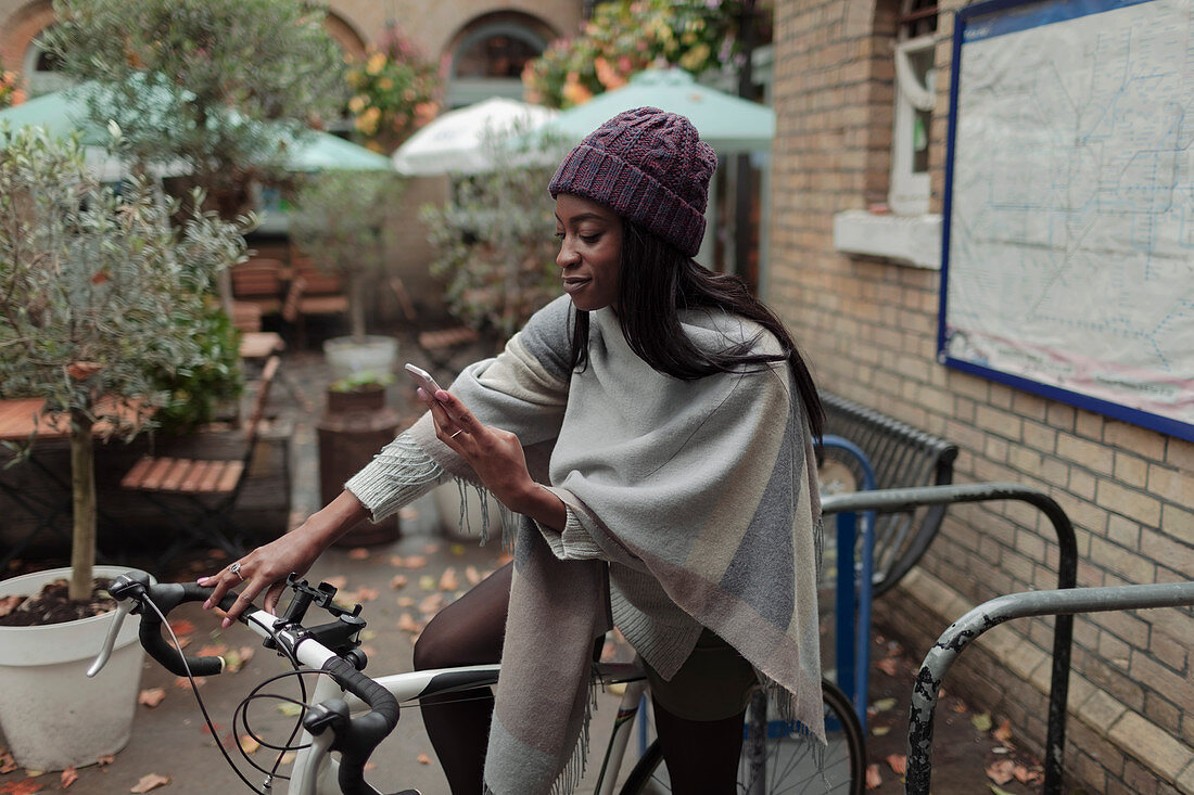 Young woman with smartphone on bicycle outside sidewalk cafe