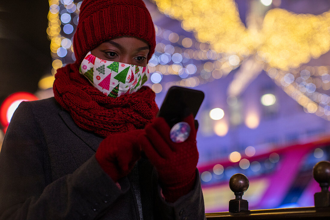 Woman in Christmas face mask and scarf using smartphone