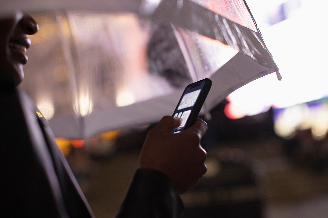 Young woman using smartphone under umbrella at night