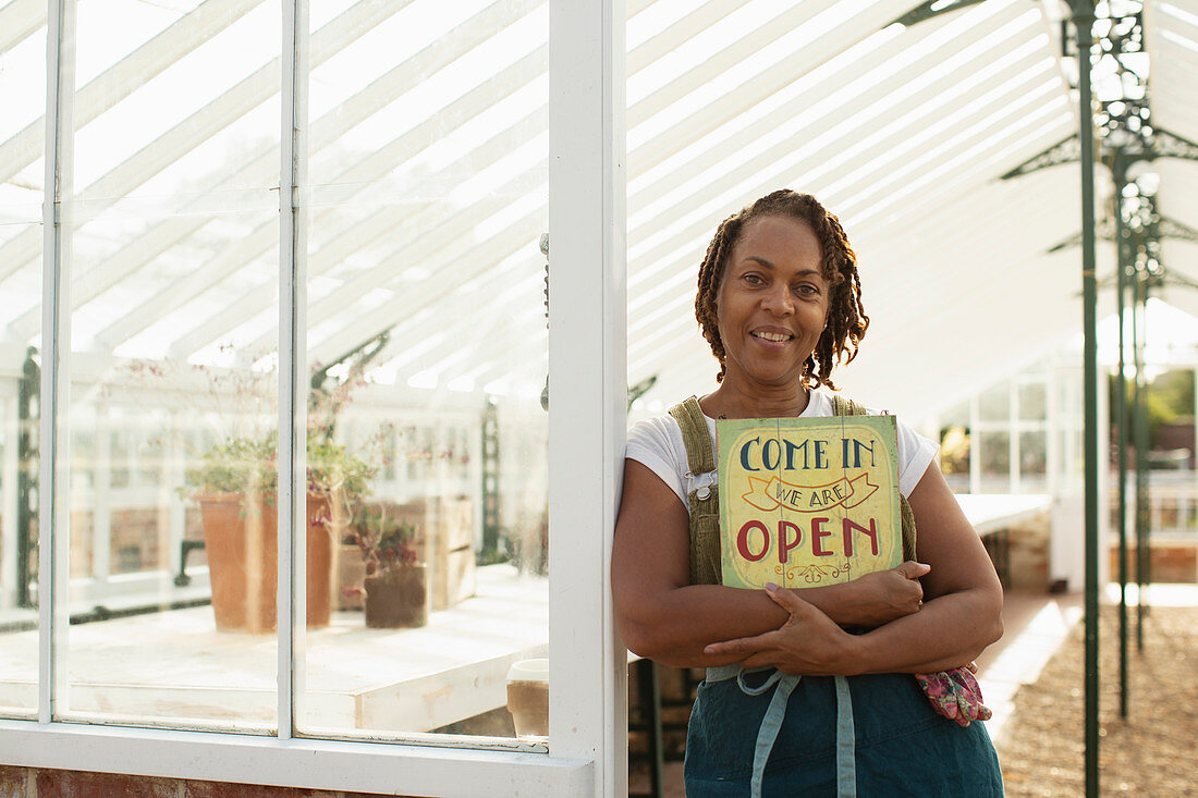 Female garden shop owner with open sign in greenhouse