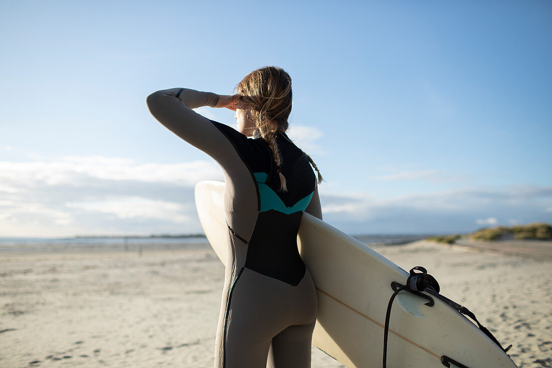 Female surfer with surfboard looking away on sunny beach