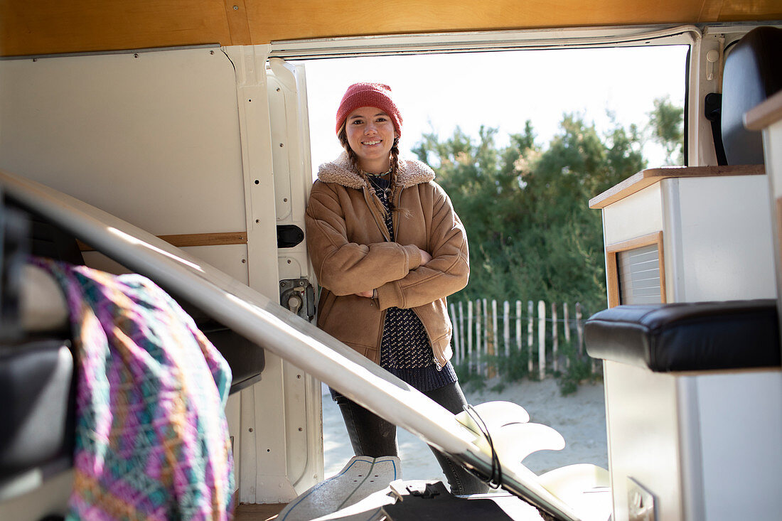 Happy young female surfer in sunny camper van doorway