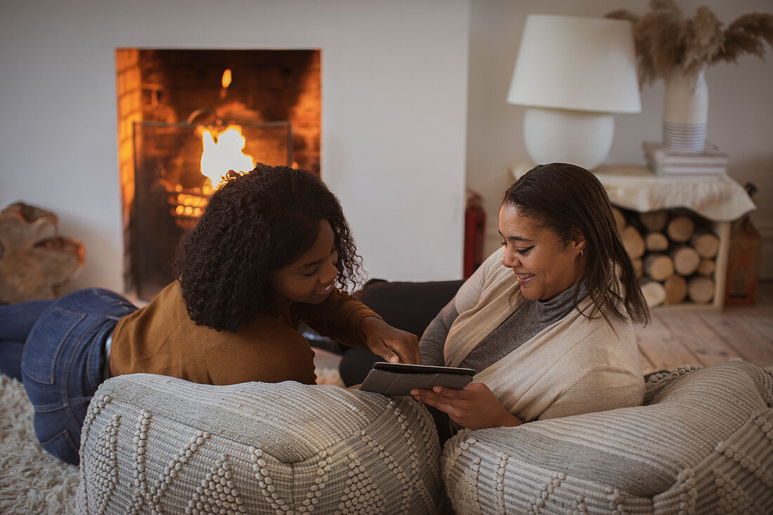 Mother and daughter using digital tablet near fireplace