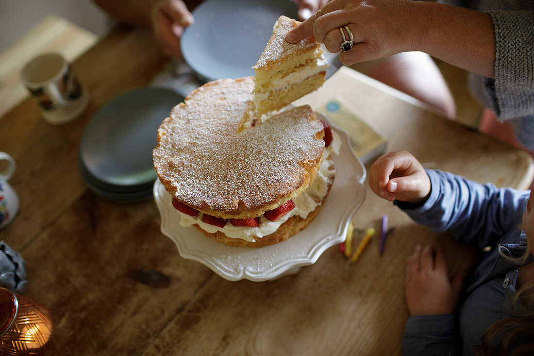 Mother slicing and serving homemade strawberry cake