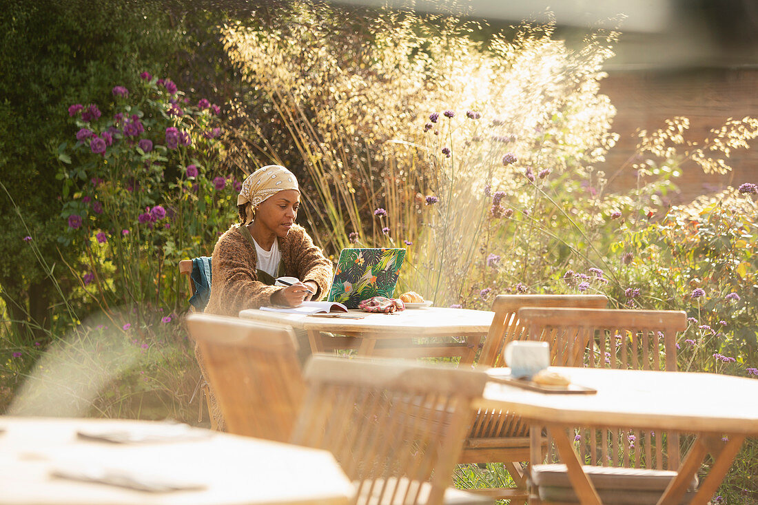 Woman working at laptop on sunny garden cafe patio