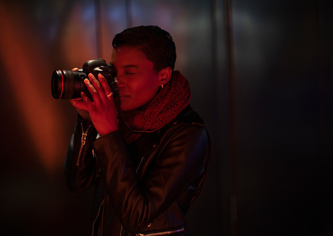 Young woman using digital camera in dark red light