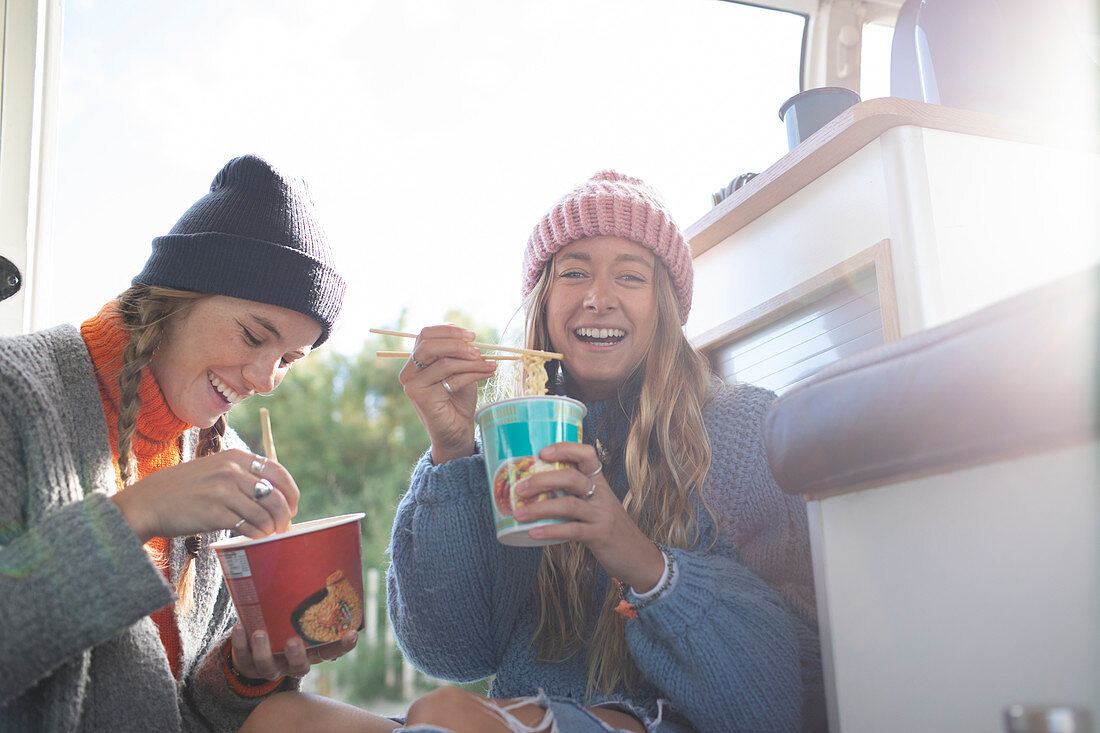 Happy young women eating instant noodles in camper van