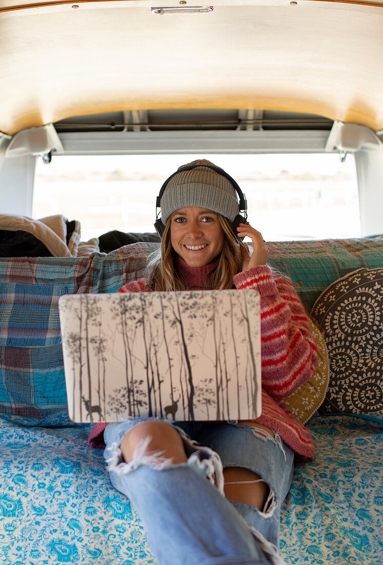 Happy young woman with headphones and laptop in camper van