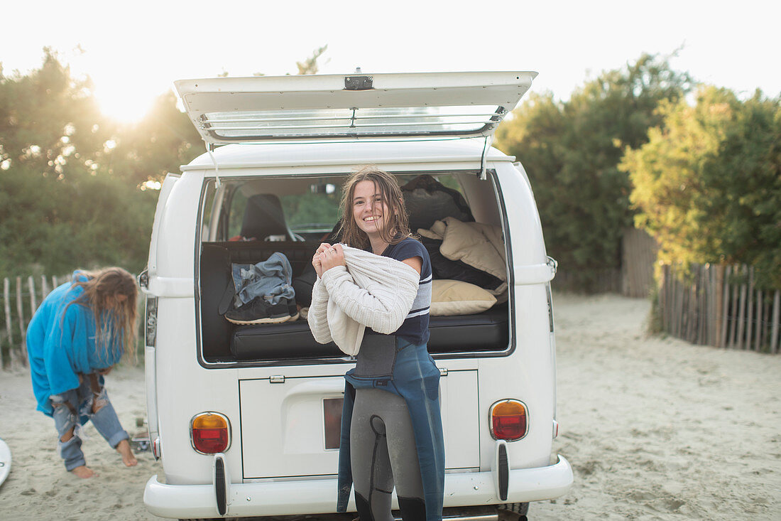 Young female surfer putting on sweater at sunny camper van