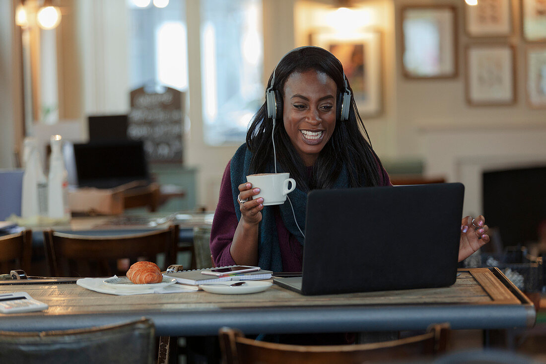 Woman with headphones drinking coffee and working at laptop