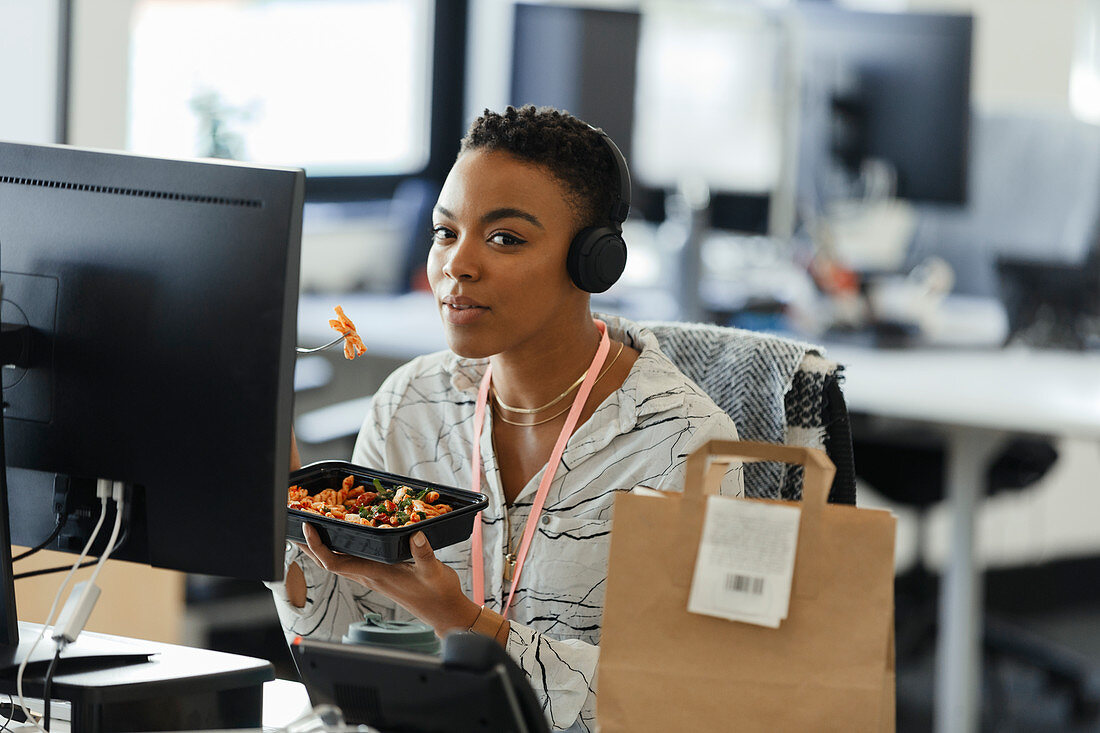 Confident businesswoman eating takeout lunch at office desk
