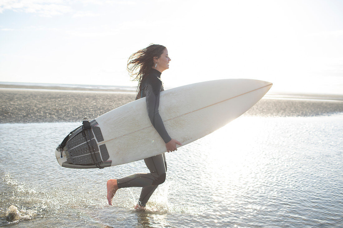 Happy female surfer running with surfboard on beach