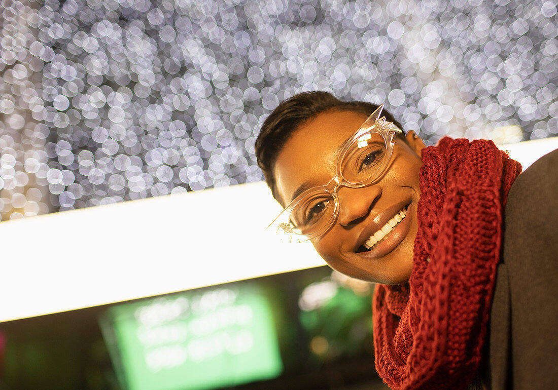 Happy young woman in funky eyeglasses and scarf below lights