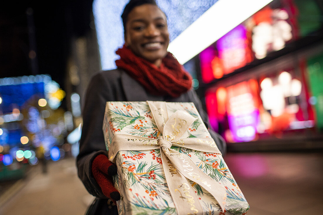 Happy woman with Christmas gift on city street at night