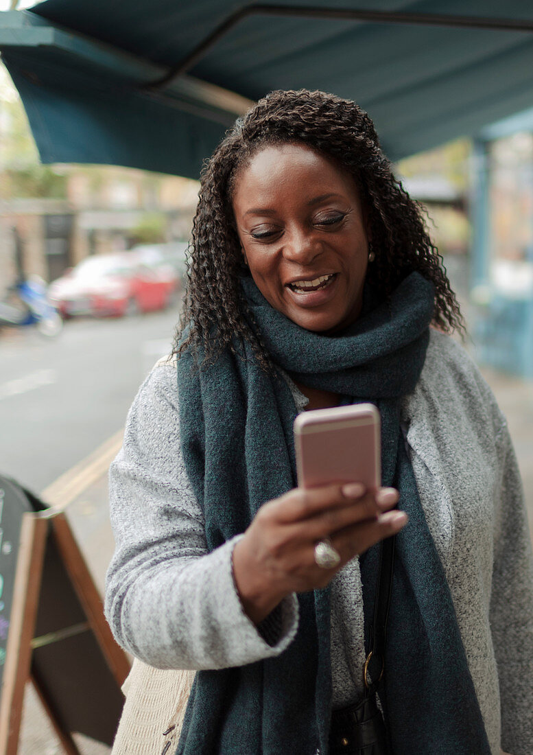 Happy woman in scarf using smart phone on sidewalk