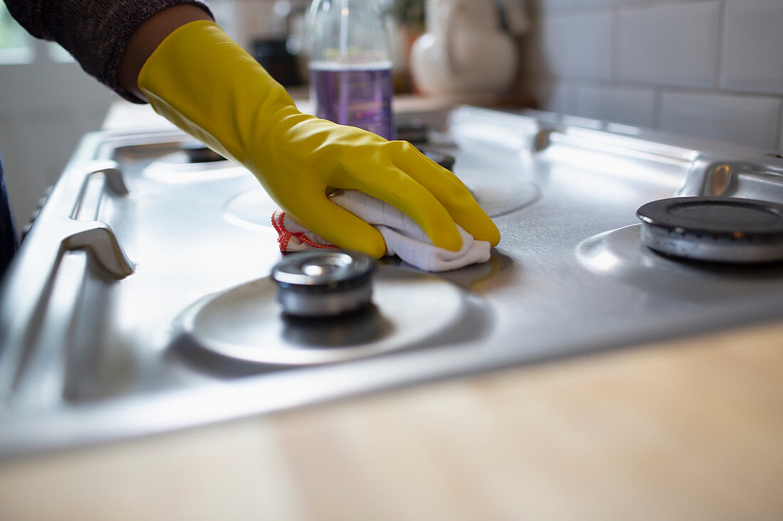 Woman in rubber gloves cleaning kitchen stove with rag