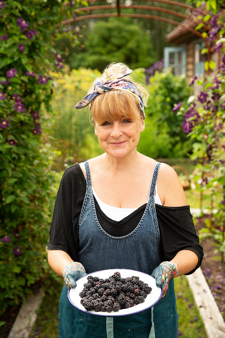 Proud woman with fresh harvested blackberries in garden