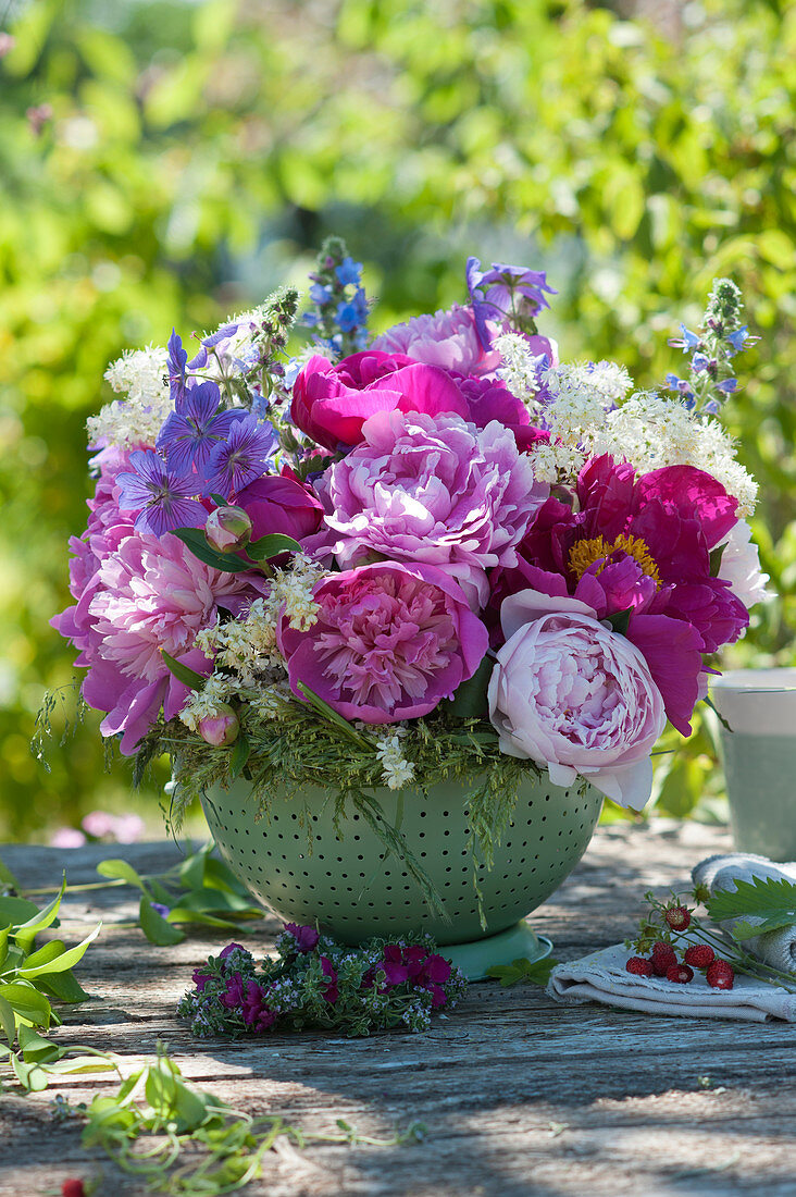 Arrangement with peonies, cranesbills, elderflowers and ox tongue in the kitchen sieve