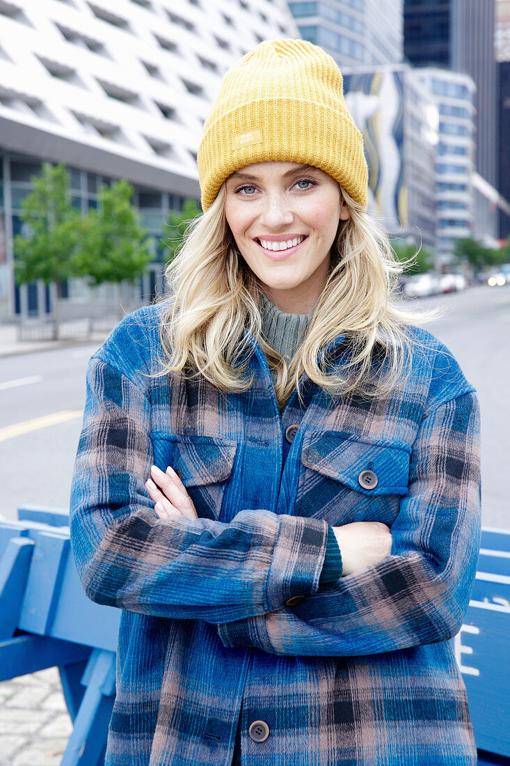 A young blonde woman wearing a mustard-yellow knitted hat and a blue-checked jacket