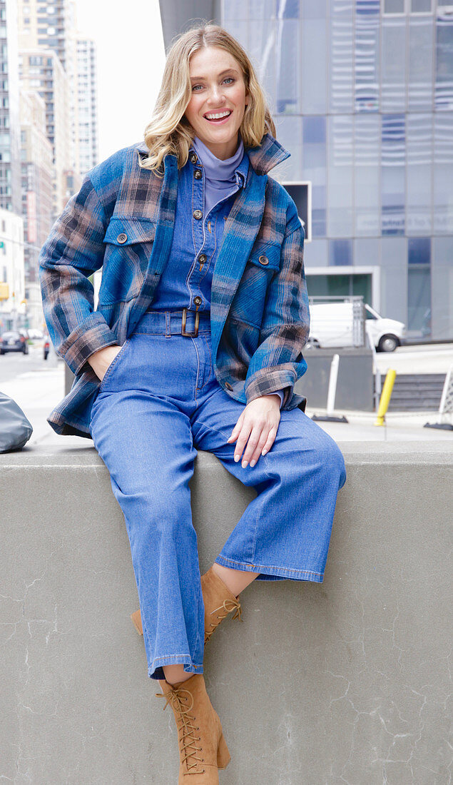 A young blonde woman wearing blue denim dungarees and a checked jacket