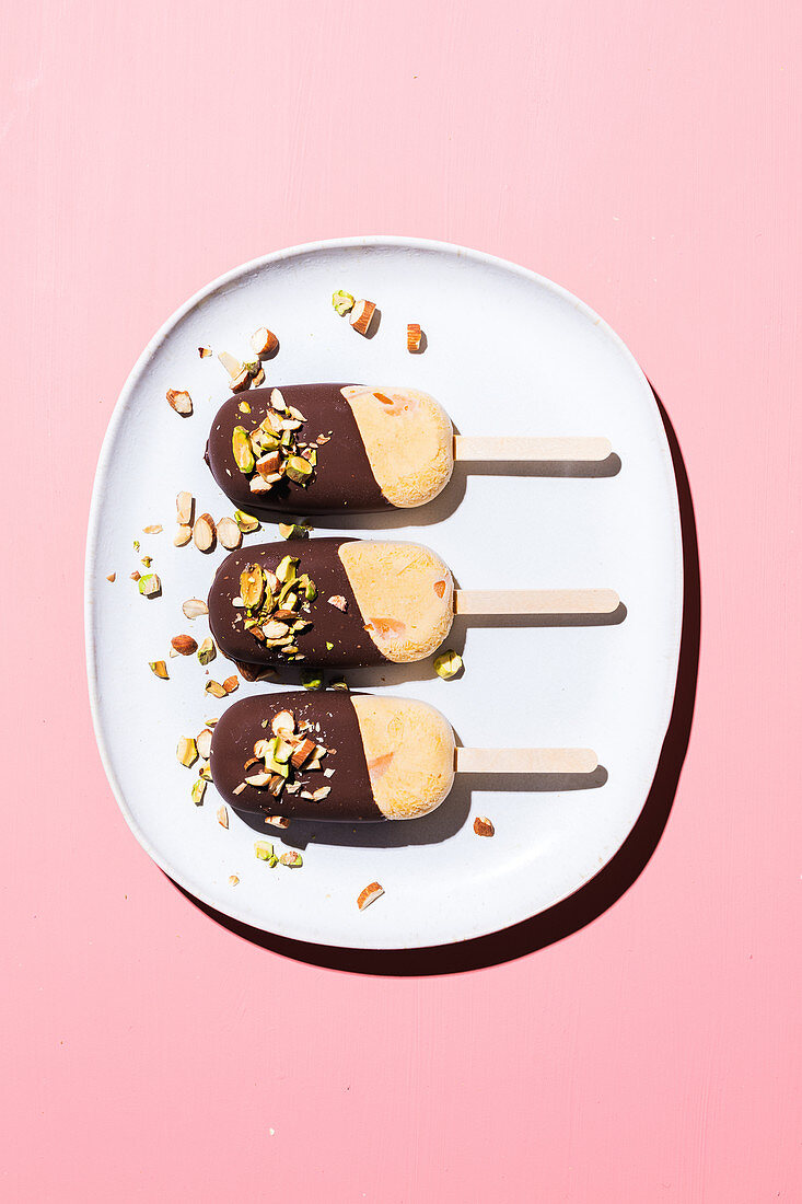 Orange ice cream on stick with chocolate icing and nuts