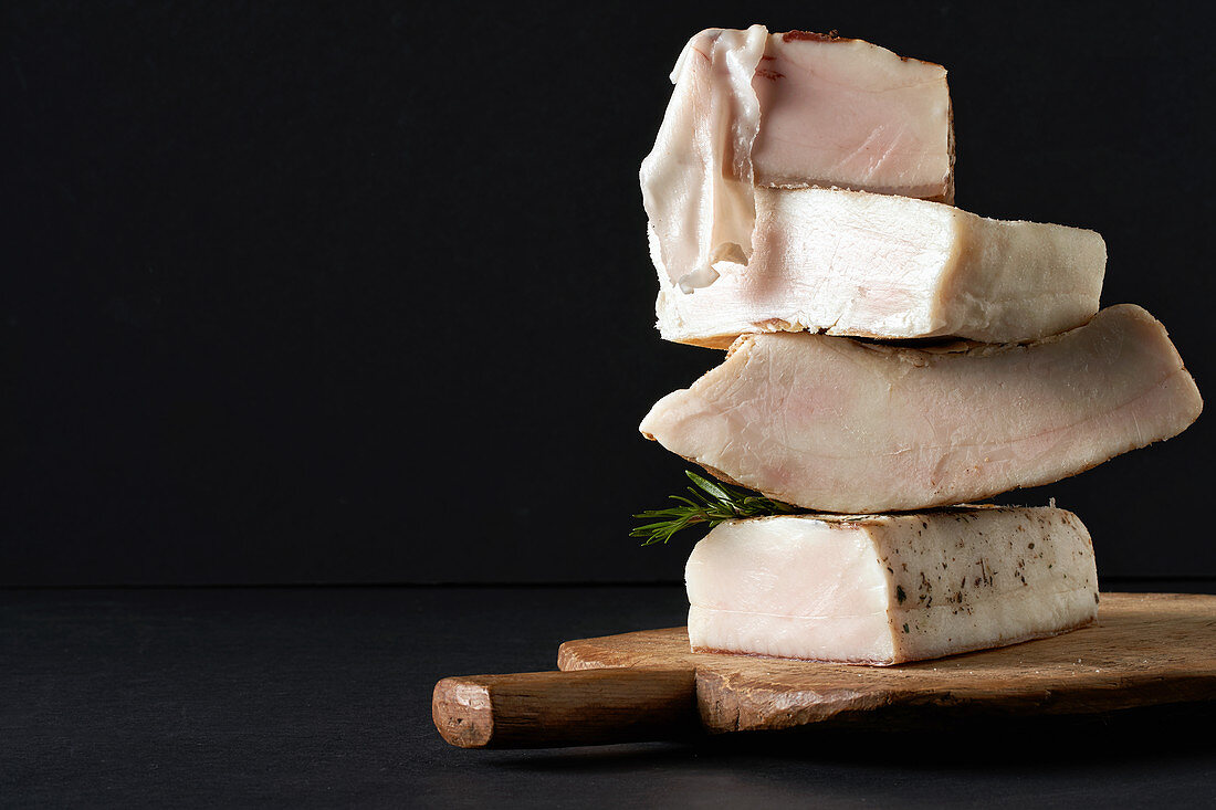 Various lardo pieces stacked on a wooden board