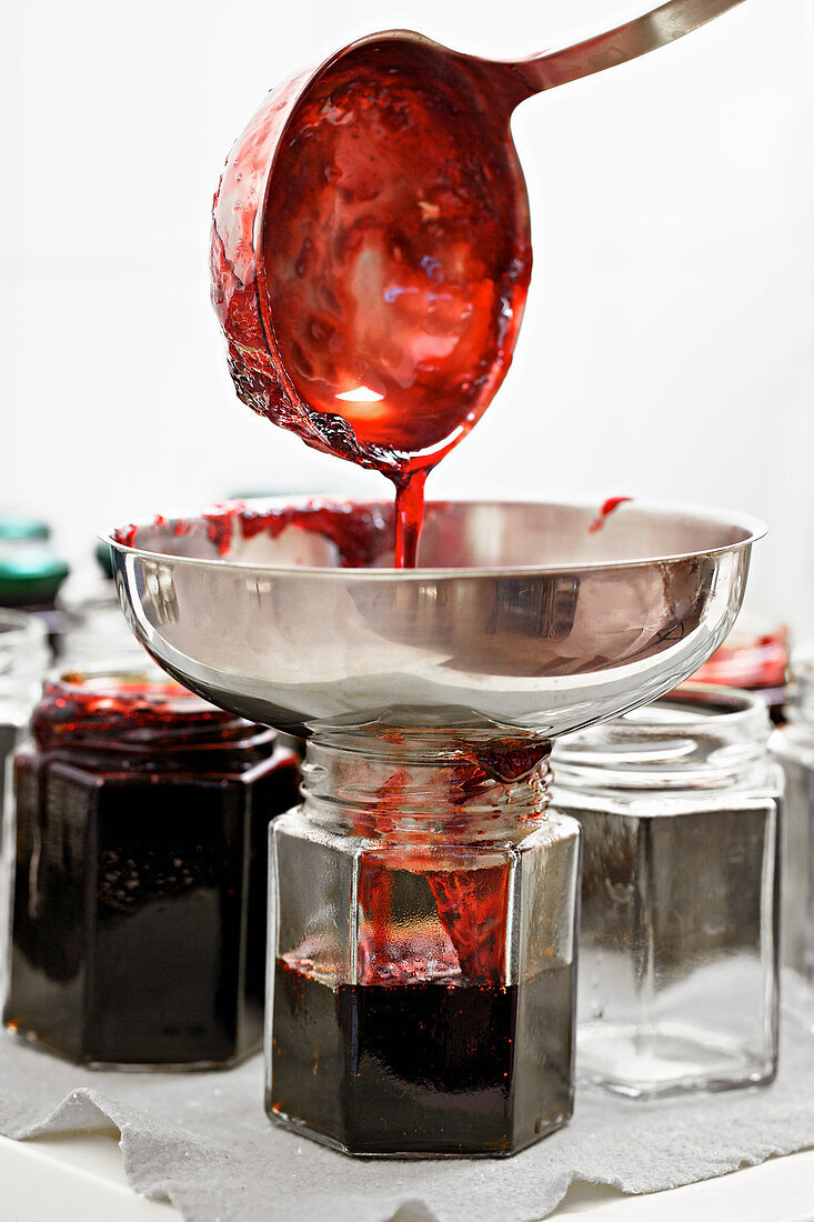 Pouring blackberry jam into glasses with a ladle and funnel
