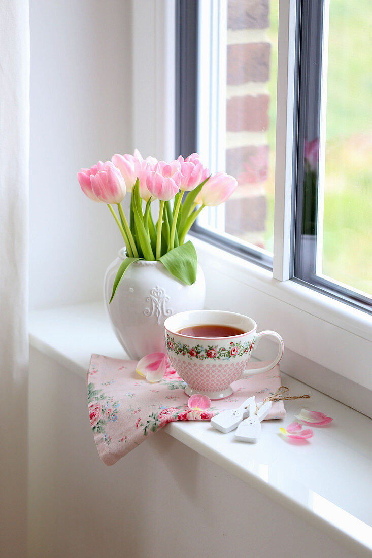 Vase mit Tulpenstrauß und Teetasse auf Fensterbank