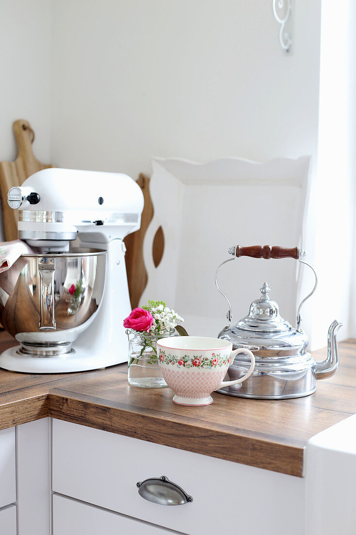 Tea kettle, tea cups and a small bouquet of flowers next to the food processor
