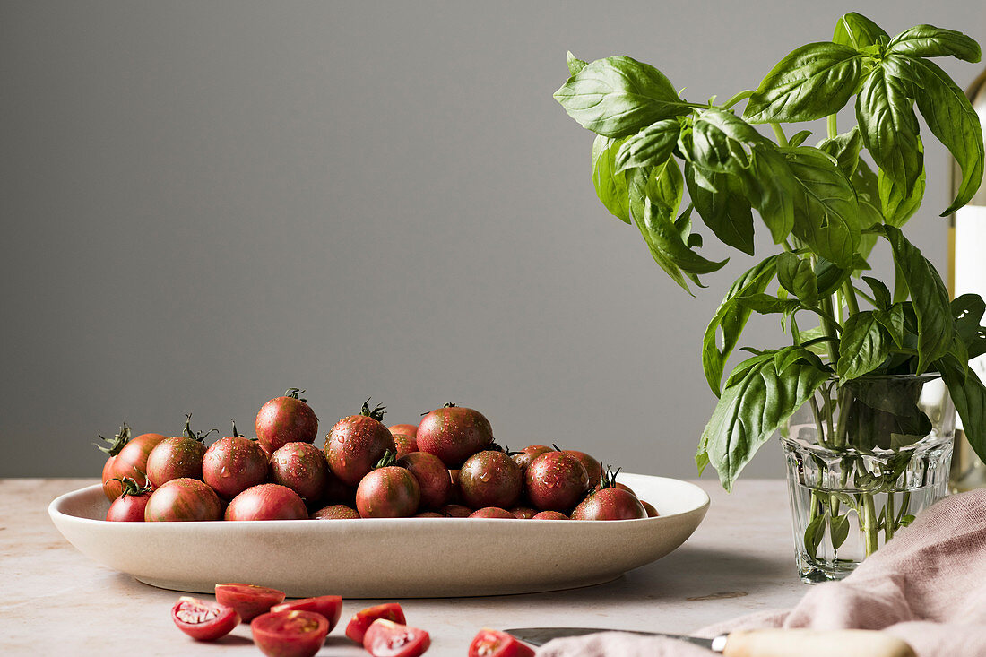 Frische Cherrytomaten in einer Schale daneben Basilikum