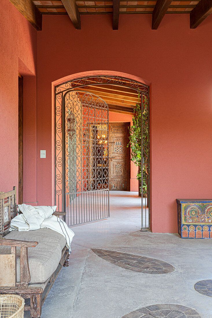 Wooden bench in anteroom with walls painted brick-red and wrought-iron gate
