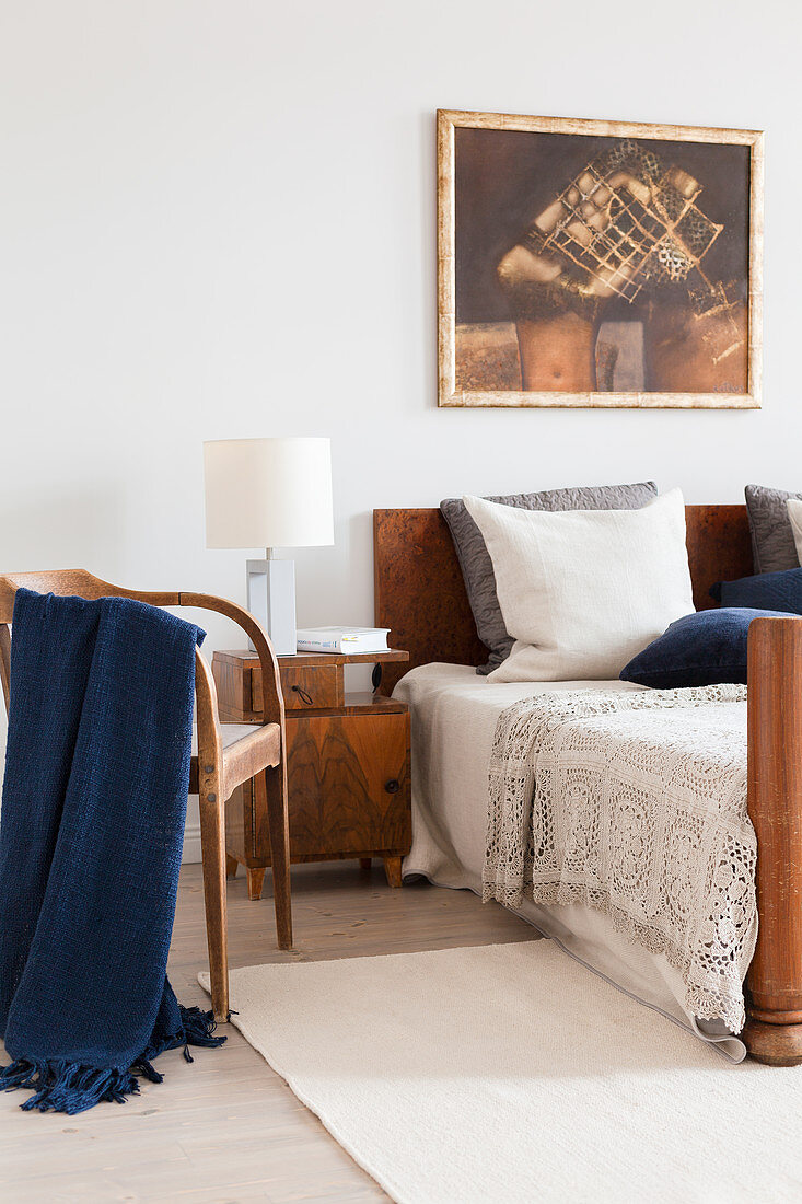 Chair and antique bedside table with lamp next to bed with wooden headboard