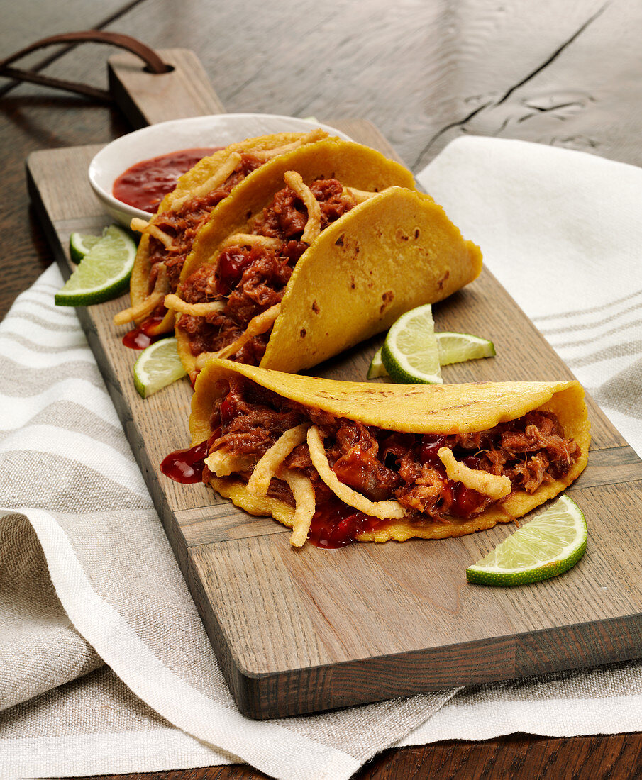 A cutting board with three Adobo Pork Tacos in corn tortillas with lime slices garnish