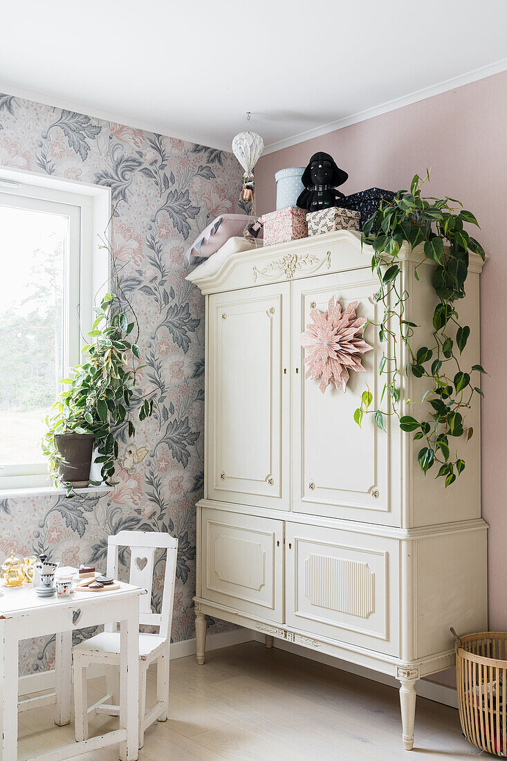 White wardrobe with indoor plant and little table with chair in a children's room