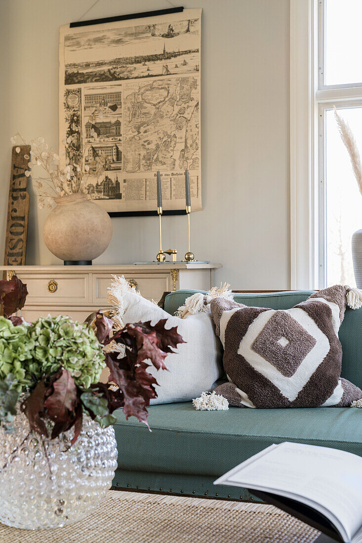 Upholstered sofa with cushions, behind it a chest of drawers and an old poster