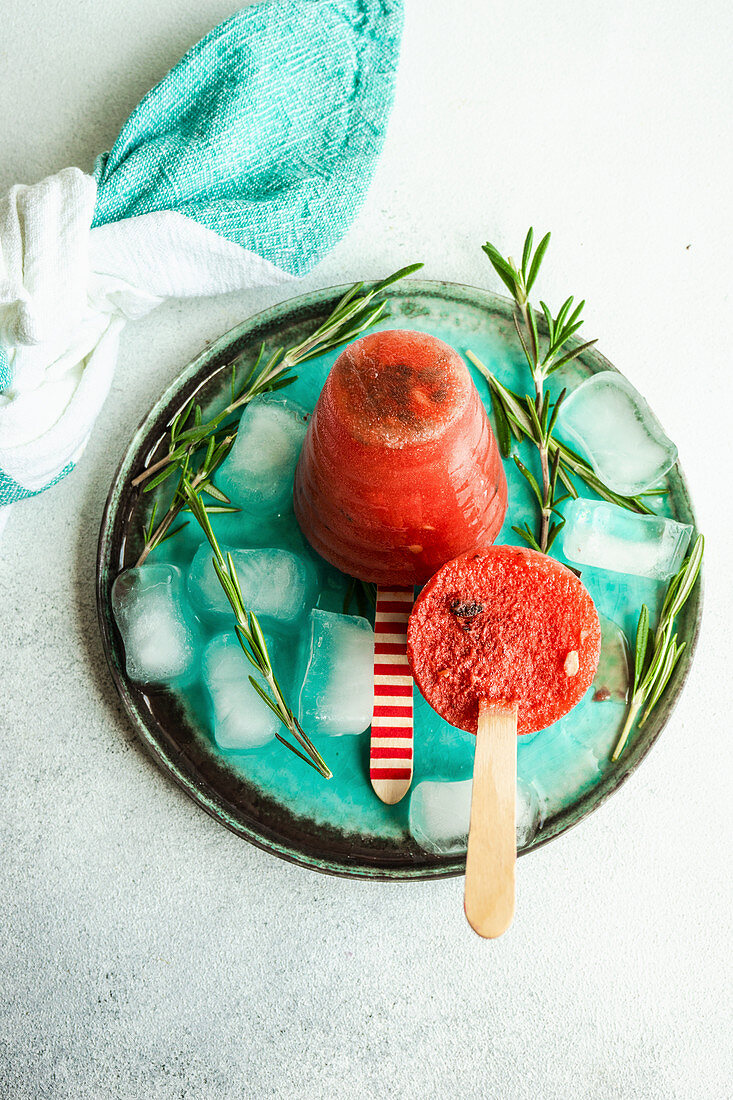 Bio-Wassermeloneneis am Stiel serviert mit Eiswürfeln und Rosmarin