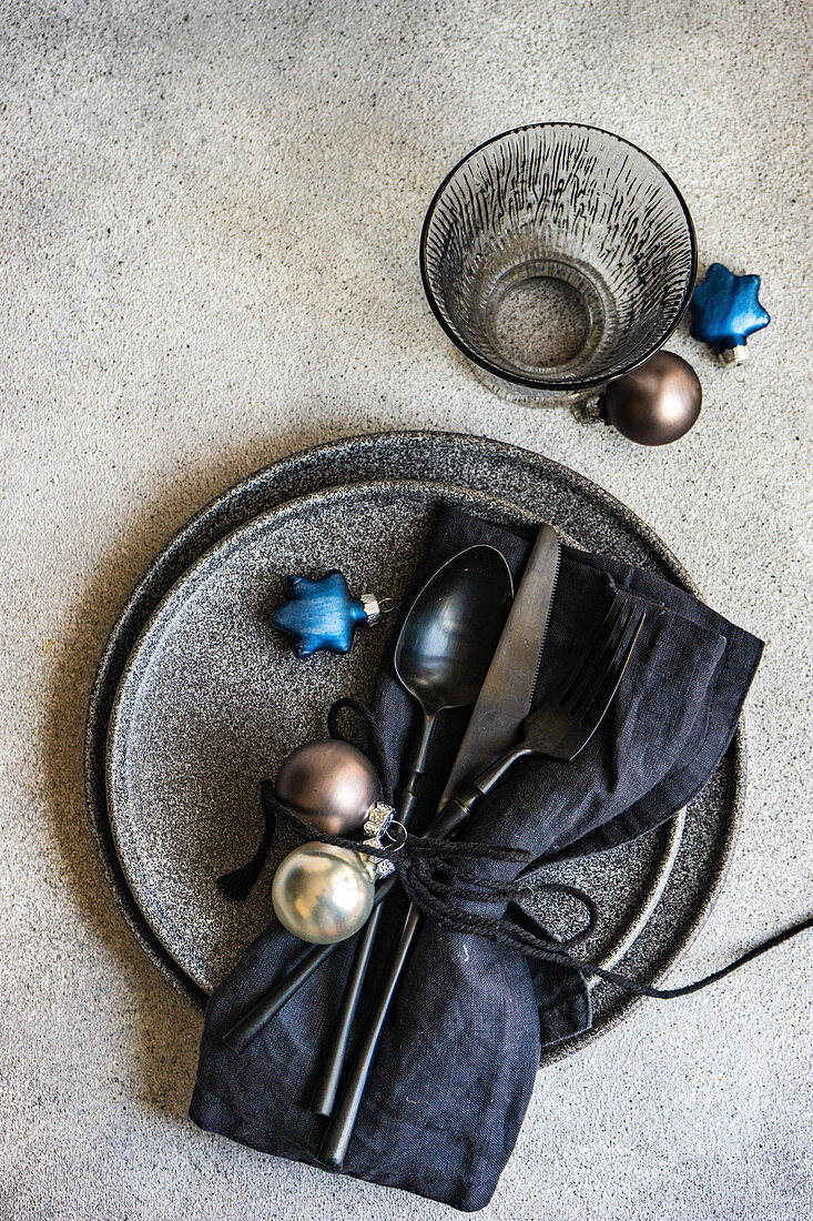 Minimalistic table setting with black stoneware and Christmas decoration on grey concrete background