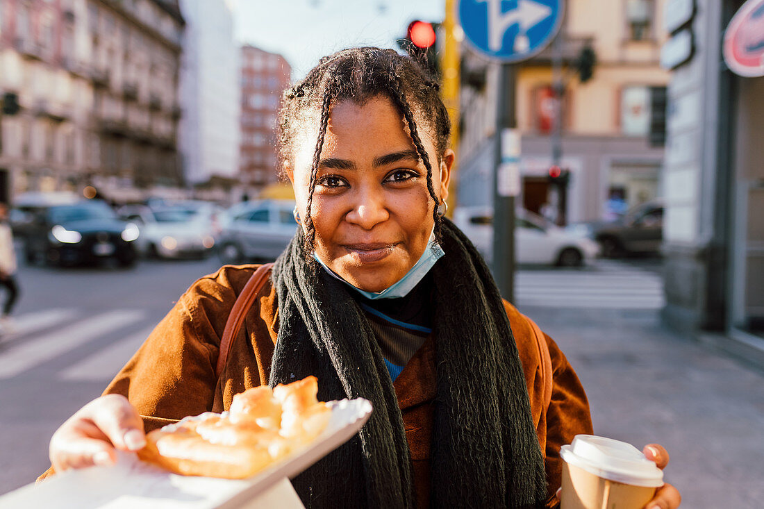 Lächelnde junge Frau mit Snack auf der Straße, Italien